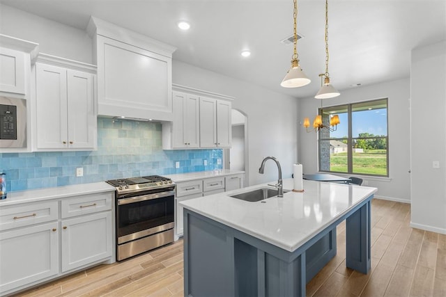 kitchen with light wood-type flooring, gas range, white cabinetry, hanging light fixtures, and an island with sink