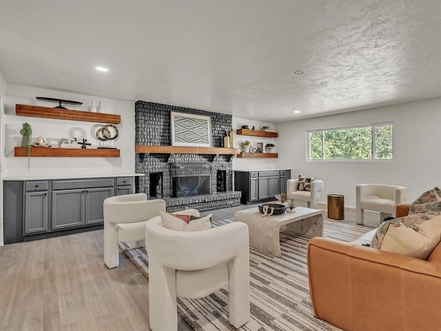 living room featuring a textured ceiling, light wood-type flooring, and a brick fireplace