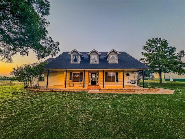 back house at dusk with a lawn and covered porch