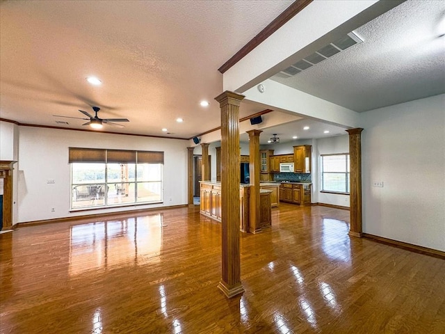 living room featuring dark hardwood / wood-style floors, ceiling fan, ornamental molding, a textured ceiling, and decorative columns