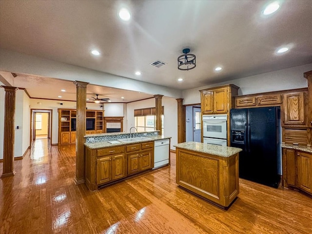 kitchen featuring ornate columns, dishwasher, sink, black fridge, and a kitchen island