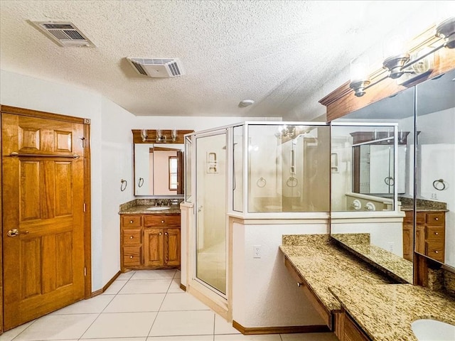 bathroom featuring tile patterned floors, vanity, a shower with shower door, and a textured ceiling