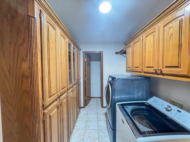 clothes washing area with washing machine and dryer, light tile patterned floors, and cabinets