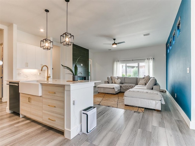 kitchen featuring sink, pendant lighting, a center island with sink, light hardwood / wood-style flooring, and black dishwasher