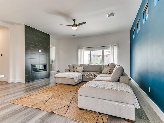 living room featuring hardwood / wood-style floors, ceiling fan, tile walls, and a tile fireplace