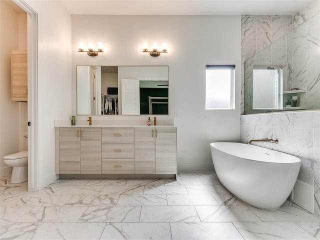 bathroom featuring a bath, vanity, toilet, and tile walls