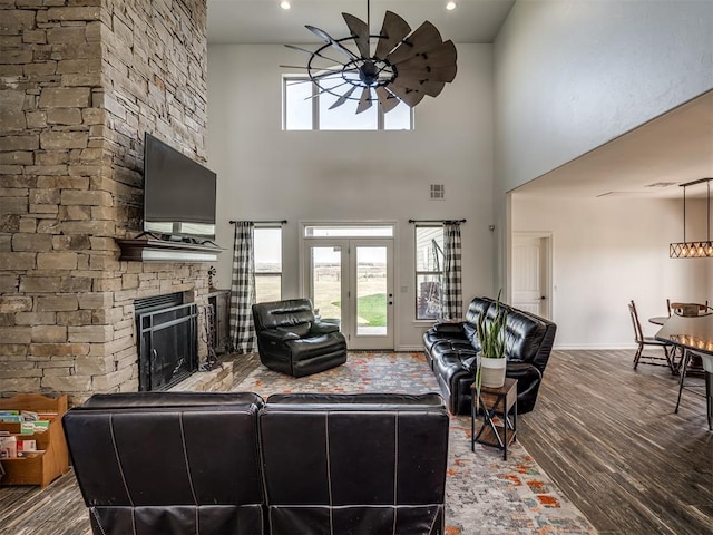 living room featuring ceiling fan, a fireplace, a towering ceiling, and wood-type flooring