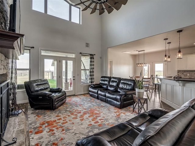 living room featuring a healthy amount of sunlight, a stone fireplace, a towering ceiling, and french doors