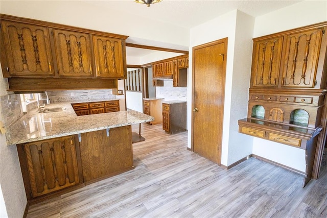 kitchen with backsplash, sink, light hardwood / wood-style floors, a kitchen bar, and kitchen peninsula