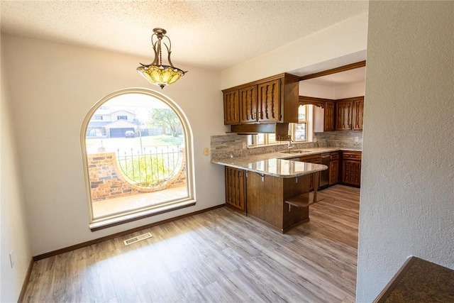 kitchen featuring kitchen peninsula, light hardwood / wood-style flooring, hanging light fixtures, and a healthy amount of sunlight