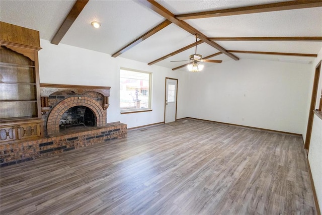 unfurnished living room featuring a textured ceiling, ceiling fan, lofted ceiling with beams, hardwood / wood-style flooring, and a fireplace