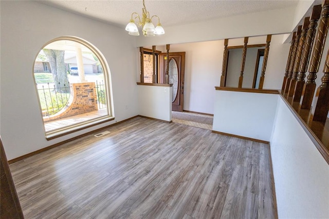 unfurnished room featuring hardwood / wood-style floors, a textured ceiling, and a notable chandelier