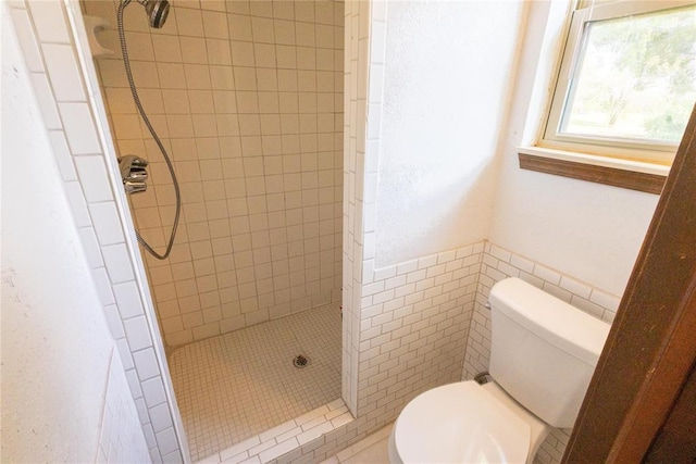 bathroom with toilet, a tile shower, and tile walls