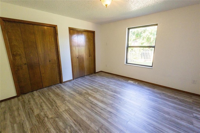 unfurnished bedroom with a textured ceiling, hardwood / wood-style floors, and two closets