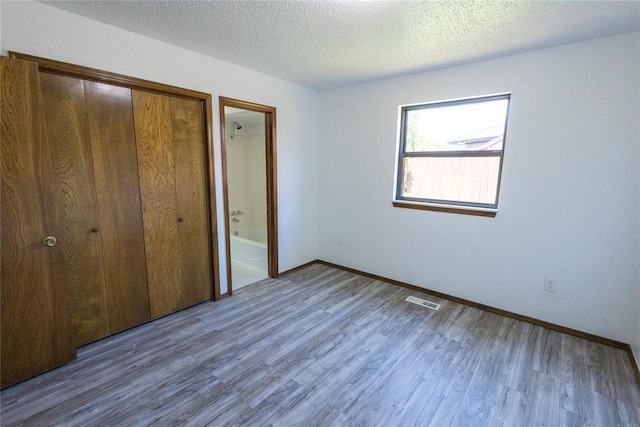 unfurnished bedroom featuring a closet, hardwood / wood-style floors, ensuite bathroom, and a textured ceiling