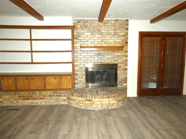 unfurnished living room with hardwood / wood-style floors, beamed ceiling, a textured ceiling, and a brick fireplace