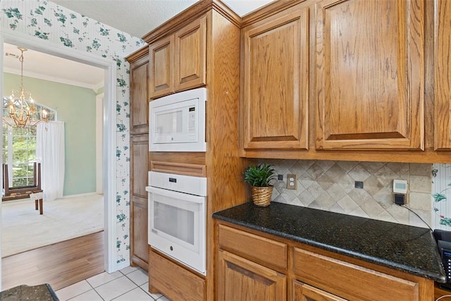 kitchen with white appliances, an inviting chandelier, crown molding, light hardwood / wood-style flooring, and dark stone countertops