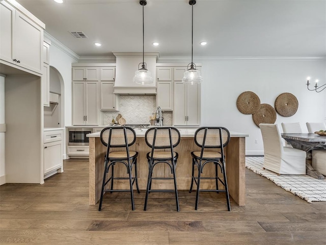 kitchen featuring decorative light fixtures, dark hardwood / wood-style flooring, an island with sink, and a breakfast bar