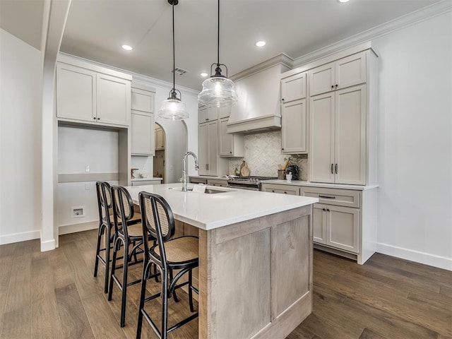 kitchen with gas range, sink, decorative light fixtures, dark hardwood / wood-style floors, and an island with sink