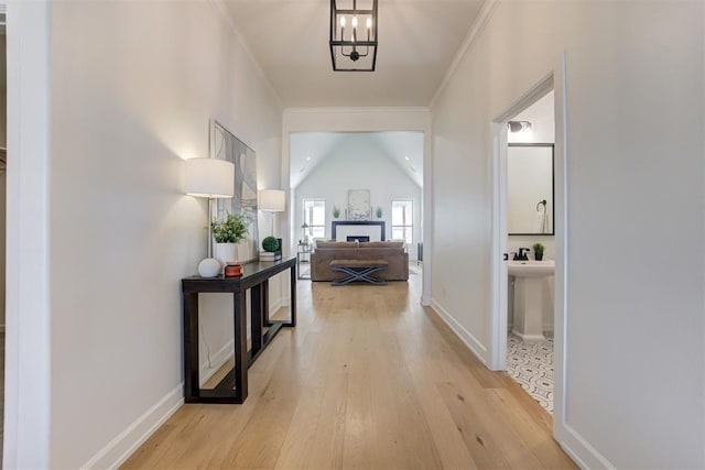 hall featuring lofted ceiling, ornamental molding, a notable chandelier, and light wood-type flooring