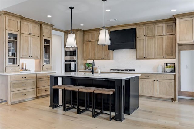 kitchen with ventilation hood, a center island with sink, sink, light hardwood / wood-style flooring, and stainless steel appliances