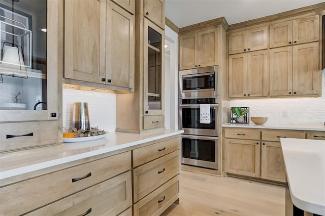 kitchen with light brown cabinets, hanging light fixtures, light hardwood / wood-style flooring, backsplash, and appliances with stainless steel finishes