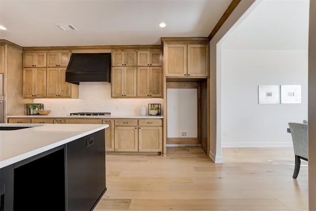 kitchen with stainless steel gas stovetop, custom exhaust hood, decorative backsplash, light wood-type flooring, and ornamental molding