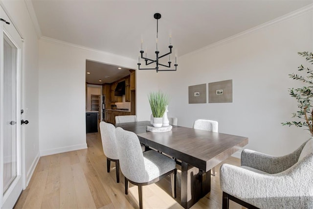 dining space with light wood-type flooring, ornamental molding, and a chandelier