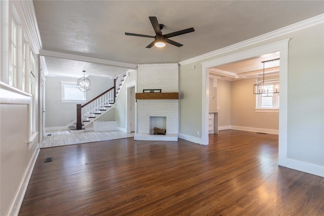 unfurnished living room with a brick fireplace, dark hardwood / wood-style flooring, ceiling fan with notable chandelier, and ornamental molding