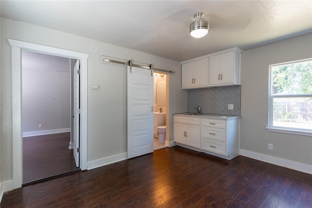 kitchen with white cabinets, decorative backsplash, a barn door, and dark wood-type flooring