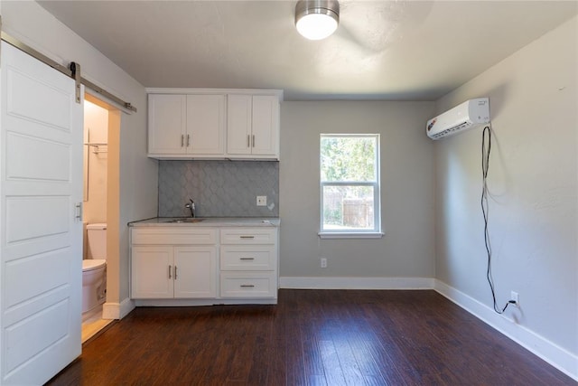 kitchen featuring tasteful backsplash, a wall unit AC, dark wood-type flooring, a barn door, and white cabinets