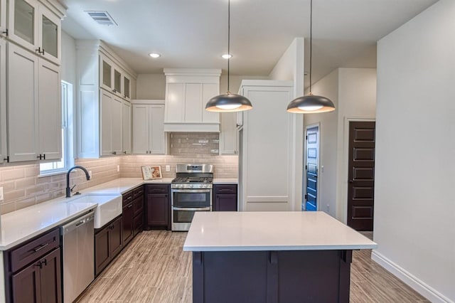 kitchen with decorative light fixtures, stainless steel appliances, white cabinetry, and light hardwood / wood-style floors