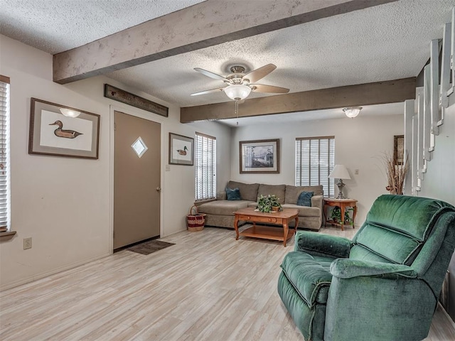 living room featuring beamed ceiling, ceiling fan, a textured ceiling, and light hardwood / wood-style flooring