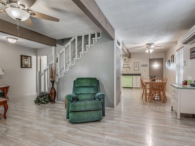 sitting room featuring a wall mounted air conditioner, a textured ceiling, light wood-type flooring, and ceiling fan