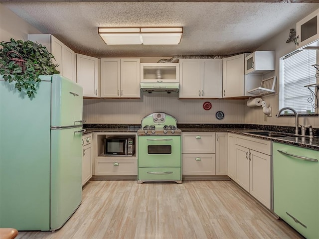 kitchen featuring white appliances, dark stone counters, white cabinets, sink, and light wood-type flooring