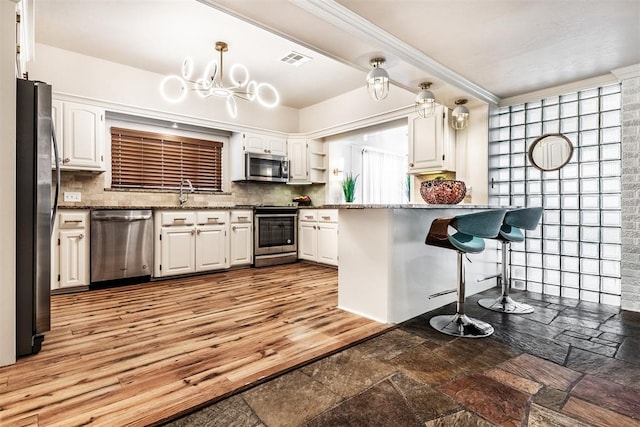 kitchen featuring tasteful backsplash, appliances with stainless steel finishes, decorative light fixtures, and white cabinets