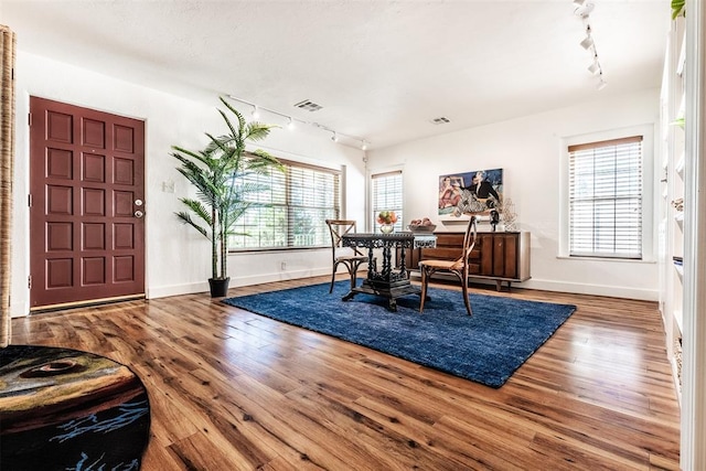 dining area featuring a healthy amount of sunlight, rail lighting, and wood-type flooring