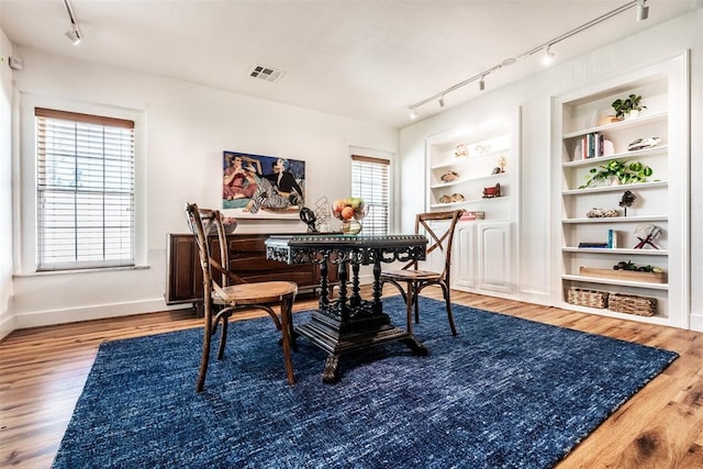 dining room featuring wood-type flooring, built in features, and track lighting