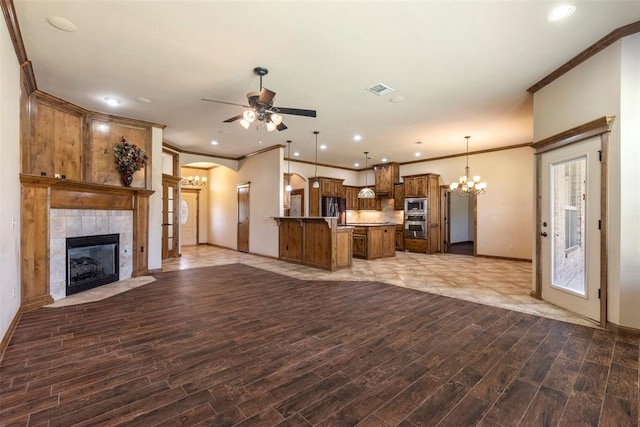 unfurnished living room featuring hardwood / wood-style floors, ceiling fan with notable chandelier, ornamental molding, and a tiled fireplace