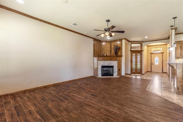 unfurnished living room with hardwood / wood-style floors, ceiling fan, ornamental molding, and a tiled fireplace