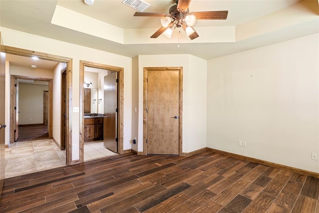 unfurnished bedroom featuring ensuite bathroom, ceiling fan, and a tray ceiling