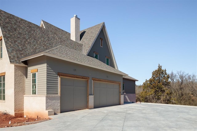 view of home's exterior with brick siding, a chimney, a shingled roof, concrete driveway, and an attached garage