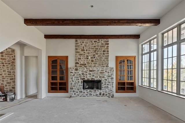 unfurnished living room with a large fireplace, plenty of natural light, and beamed ceiling