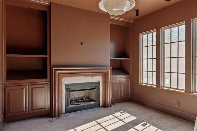 unfurnished living room with built in shelves, a high end fireplace, and baseboards