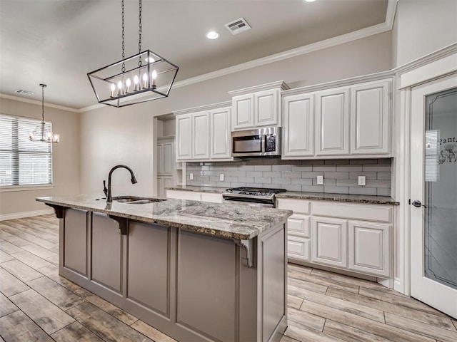 kitchen with sink, light stone counters, an island with sink, white cabinets, and appliances with stainless steel finishes