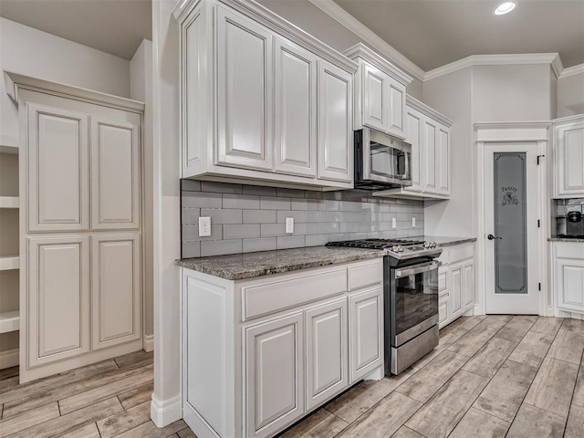 kitchen with appliances with stainless steel finishes, backsplash, white cabinetry, and light hardwood / wood-style flooring