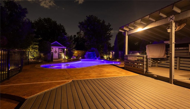 deck at night with pool water feature and a fenced in pool