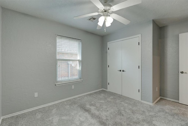 unfurnished bedroom with ceiling fan, a closet, light colored carpet, and a textured ceiling