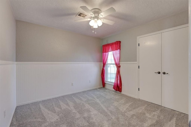 unfurnished bedroom with ceiling fan, a closet, light carpet, and a textured ceiling