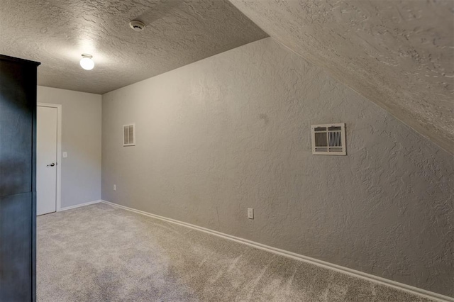 unfurnished room featuring a textured ceiling, carpet floors, and lofted ceiling